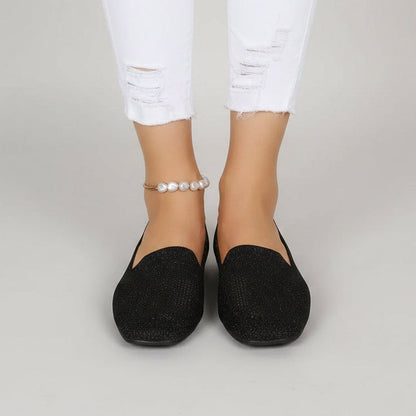 Front view of black slip-on shoes worn by a model in white ripped jeans and a pearl anklet. 2