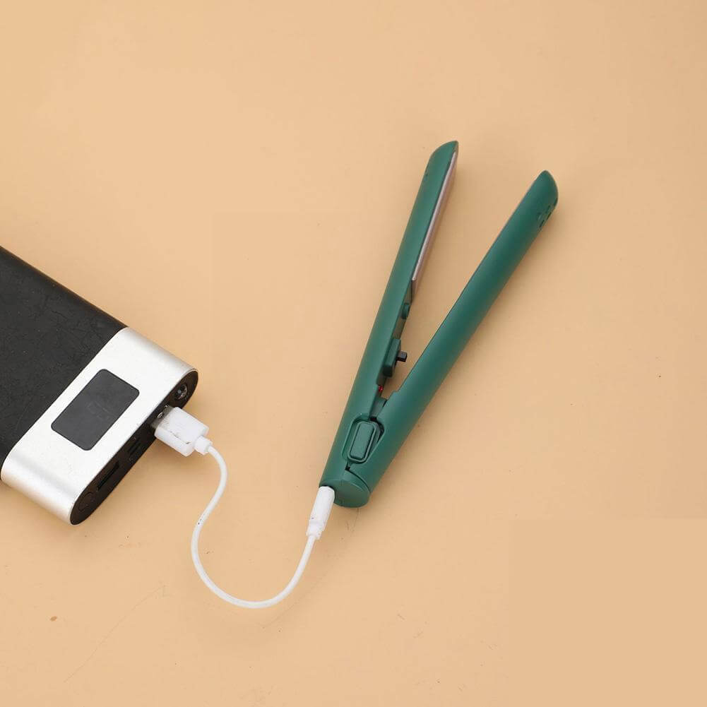 Green mini straightener open on a peach background, plugged into a black and silver power bank with a short white cable. 11