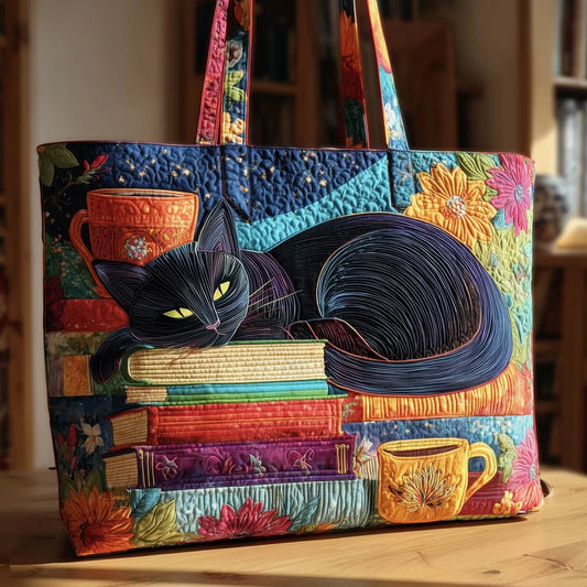 Front of the quilted tote standing on a wooden table, showing a sleeping black cat on stacked books with colourful cups and flowers. 1
