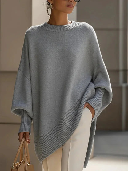 Grey jumper with ribbed neckline, cuffs and angled hem, worn with white trousers and a handbag 9