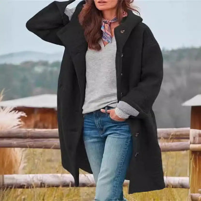 Black coat worn open over a grey top and scarf, with a wooden fence and field behind 9