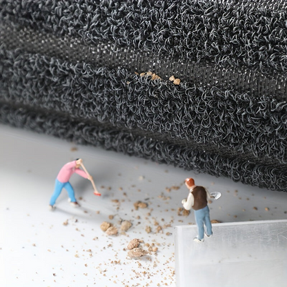 Rolled edge of the mat showing the loop pile and woven backing, with tiny figures sweeping dirt on the floor below. 6