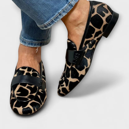 Both loafers worn with turned-up jeans, seen from the front and side, showing the animal print, black strap and low heel. 3