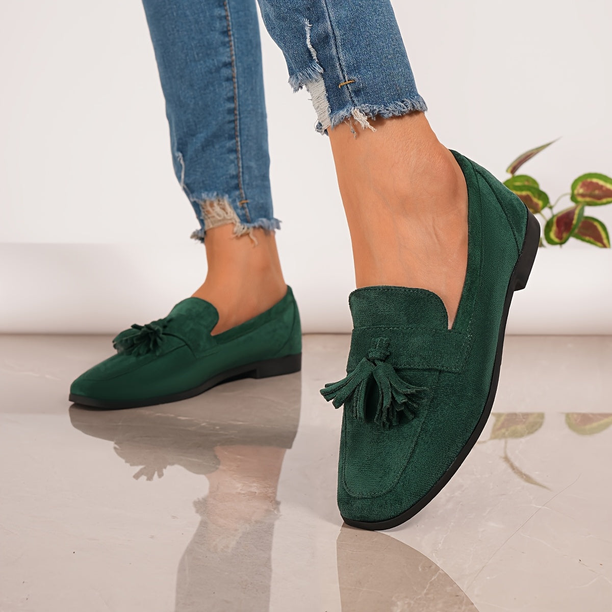 Green suede-look tasselled loafers worn with frayed-hem jeans, angled front view 2