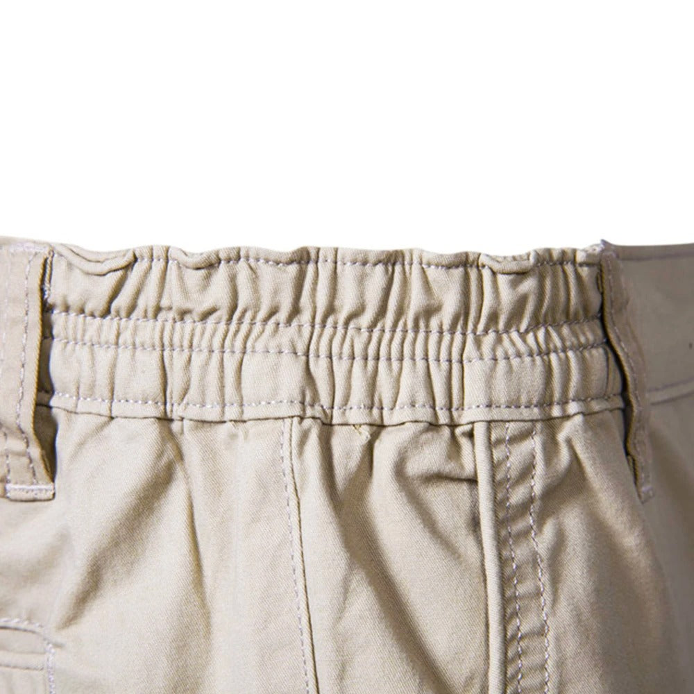 Close-up of the gathered elastic waistband at the back of the beige shorts, with contrast stitching and belt loops. 4