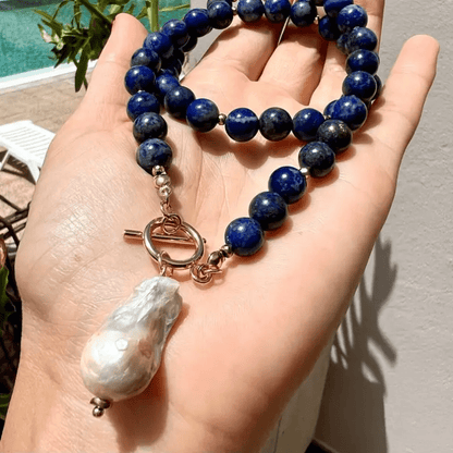 Blue bead necklace resting in an open palm outdoors, baroque pearl hanging from the toggle 2