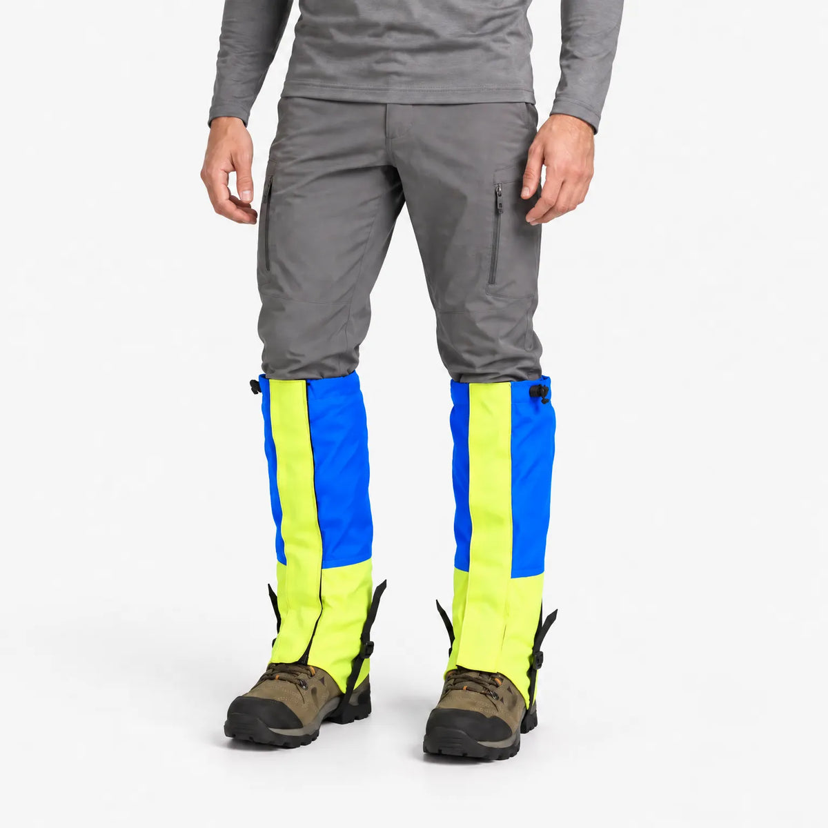 Model in grey trousers and hiking boots wearing blue and neon yellow gaiters with adjustable top toggles and instep straps. 2