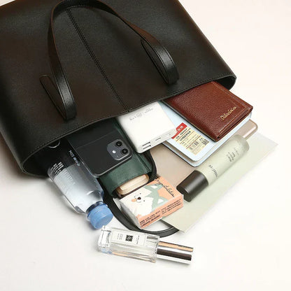 Black tote tipped on its side with a phone, wallet, bottle, perfume and other everyday items spilling out 6