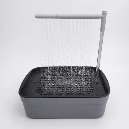 Grey bird bath with a dark slatted tray and a white overhead arm spraying a fine curtain of water, shown against plain white. 1