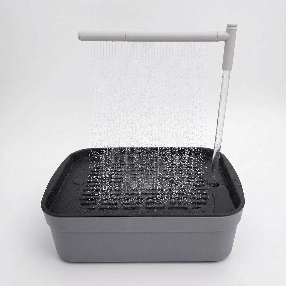 Grey rectangular bird bath on a plain white background, with an overhead arm spraying a curtain of water onto the slatted tray. 1