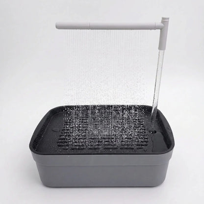 Grey rectangular bird bath on a plain white background, with an overhead arm spraying a curtain of water onto the slatted tray. 1