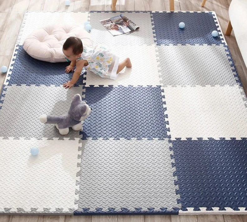 Baby crawling across a navy, grey and cream foam tile mat with a soft toy and pale blue balls. 2