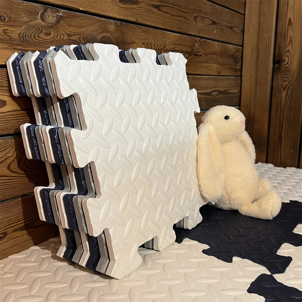 Stack of cream, navy and grey puzzle tiles leaning against a wooden wall beside a plush bunny, with a mat laid below. 3