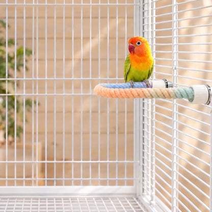 Small green and orange lovebird perched on the curved pastel rope perch, fixed inside a white cage. 2