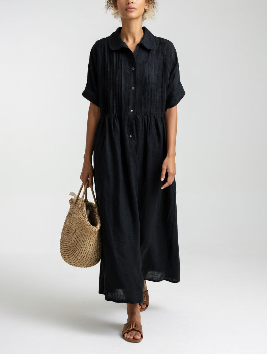Model in the black dress facing front, showing the dark buttons, pintucked bodice and gathered waist, carrying a straw tote. 7