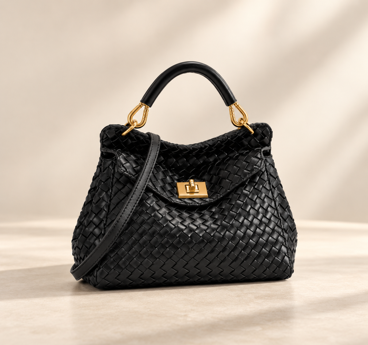 Black woven-textured version with gold turn-lock, rolled top handle and strap, on a pale studio surface 3