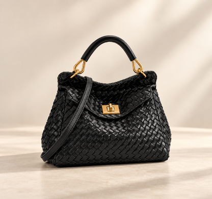 Black woven-textured version with gold turn-lock, rolled top handle and strap, on a pale studio surface 3