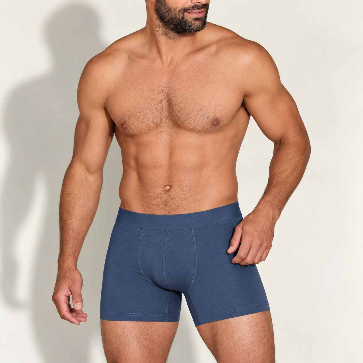 Bearded muscular model, shirtless, wearing mid-blue boxer briefs with a plain waistband and contrast-free front seams, hand resting at his hip. 1