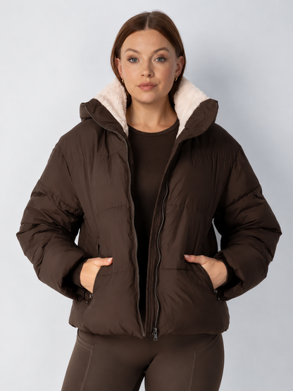 Model wears the dark brown puffer jacket open with cream fleece collar, hands in the zipped pockets 14