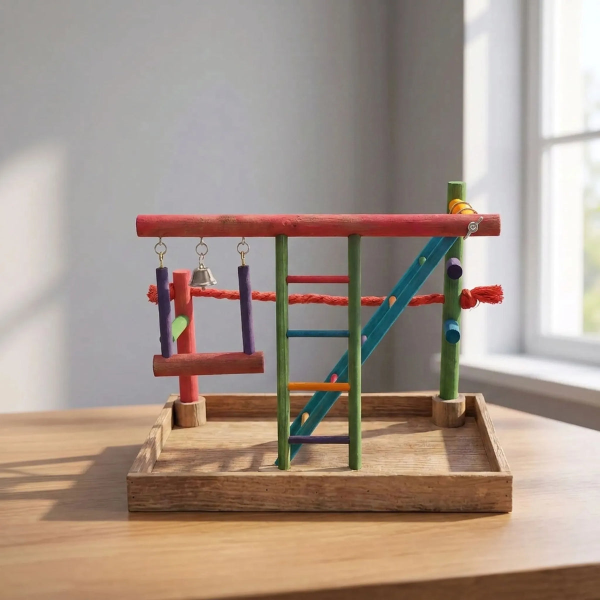 Colourful wooden bird playground standing on a wooden table beside a window, in soft daylight, with its swing, ladder and bell. 2