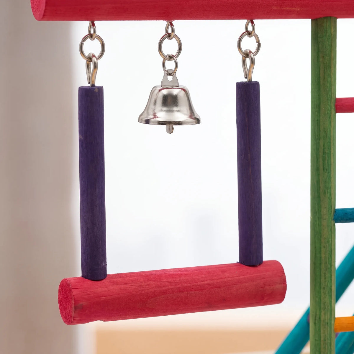 Close-up of the hanging swing with purple side posts and a red perch, with a small silver bell between the hooks. 4