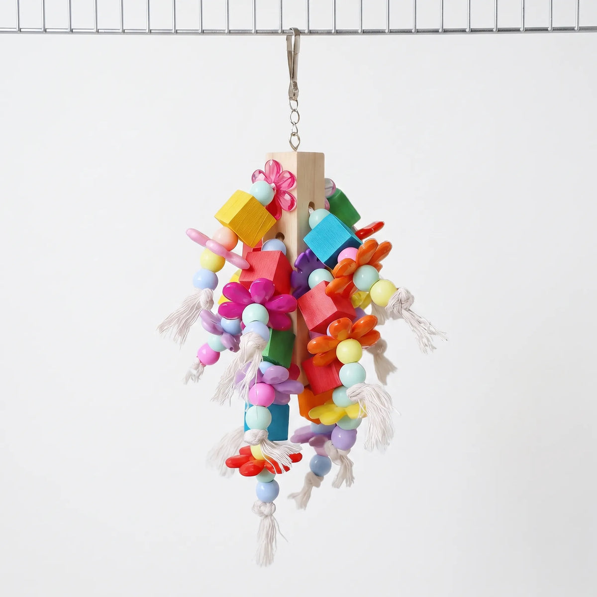 Hanging bird toy with a wooden core, coloured blocks, plastic flowers, beads and knotted cotton rope, clipped to a wire bar. 1
