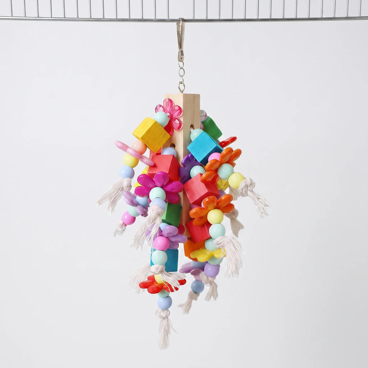 Toy hanging from a curved wire bar by its metal clip, showing flowers, blocks and beads on rope strands against a plain background. 4