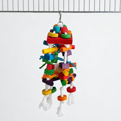 Toy of dyed wooden blocks, beads and knotted white cotton rope hanging from a metal clip on a cage bar against a plain background. 1