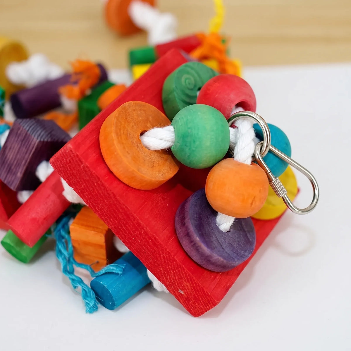 Close-up of the top of the toy, showing the red wooden plank, coloured beads and discs on white rope, and the metal clip. 4