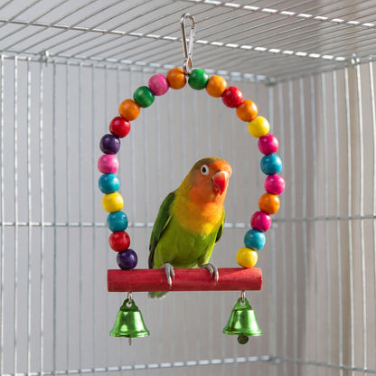 Lovebird perched on the red wooden bar of the multicoloured bead arch swing with two green bells, inside a wire cage. 2