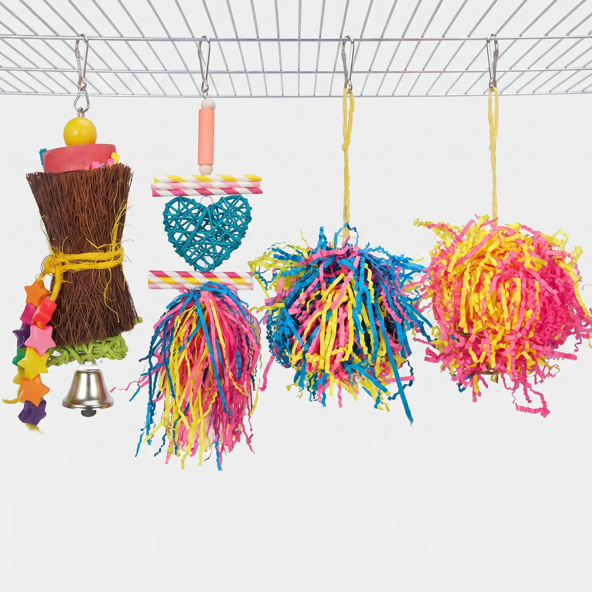 Four toys hanging from a cage roof: the fibre bundle with bell, a rattan heart with paper straws, and two shredded-paper pom-poms. 7
