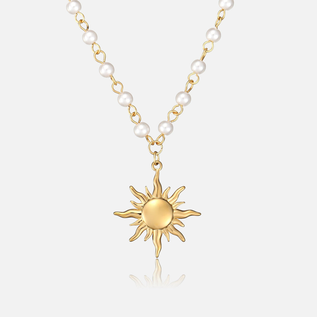 Front view of a gold-toned sun pendant with wavy rays hanging from a chain of white pearl beads on a plain background. 1