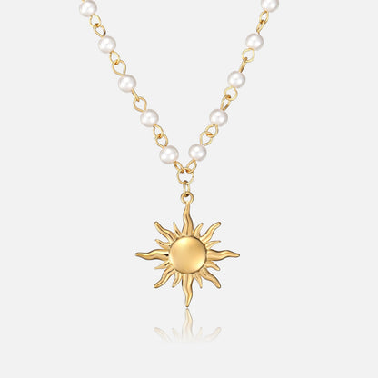 Front view of a gold-toned sun pendant with wavy rays hanging from a chain of white pearl beads on a plain background. 1