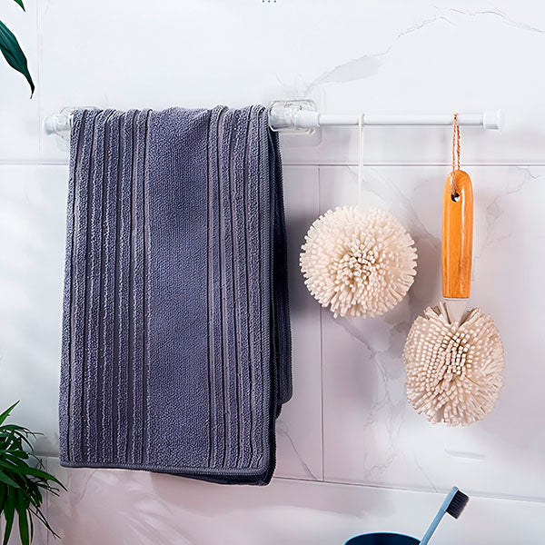White bathroom rod on clips against marble tiles, holding a grey striped towel and two fluffy hanging bath sponges. 9