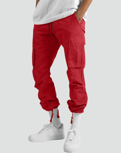 Model in red cargo trousers with hems drawn in at the ankles, worn with white socks and trainers, front view. 11