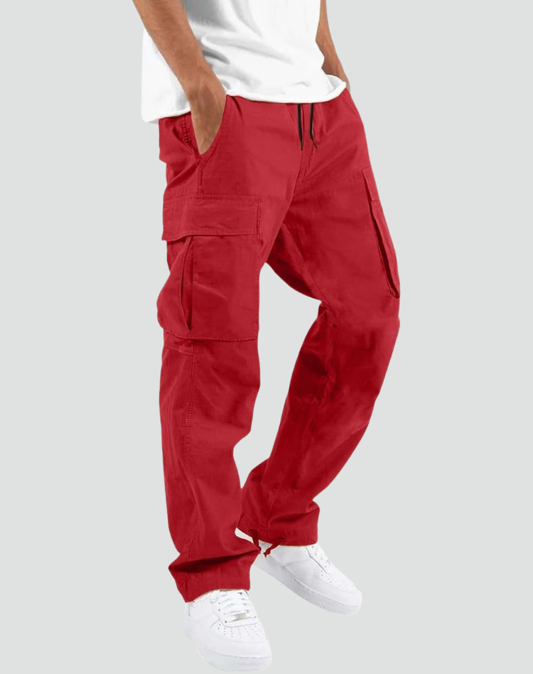 Model wearing red cargo trousers with a white t-shirt and white trainers, hand in pocket, angled side view. 10