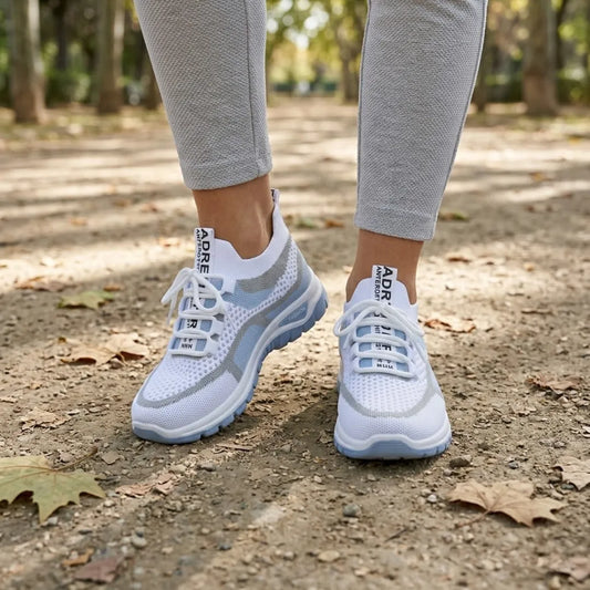 Pair of white and pale blue mesh trainers worn by a model in grey leggings, walking on a leafy park path. 2
