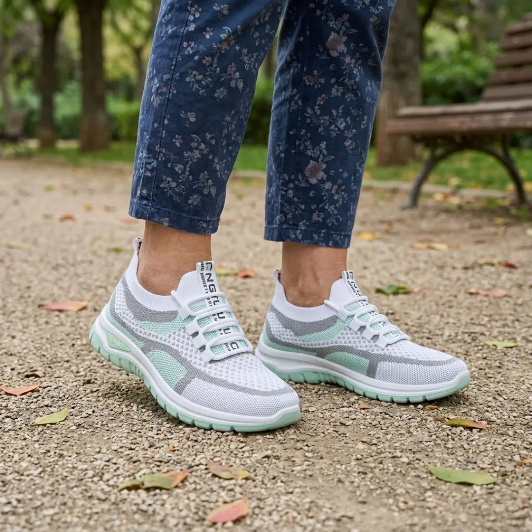 Pair of white and mint green mesh trainers worn with floral blue trousers on a gravel park path with fallen leaves. 11