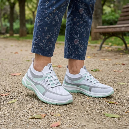 Pair of white and mint green mesh trainers worn with floral blue trousers on a gravel park path with fallen leaves. 11