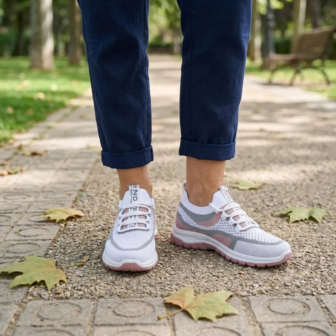 Pair of white and dusky pink mesh trainers worn with rolled navy trousers, standing on a paved park path with leaves. 20
