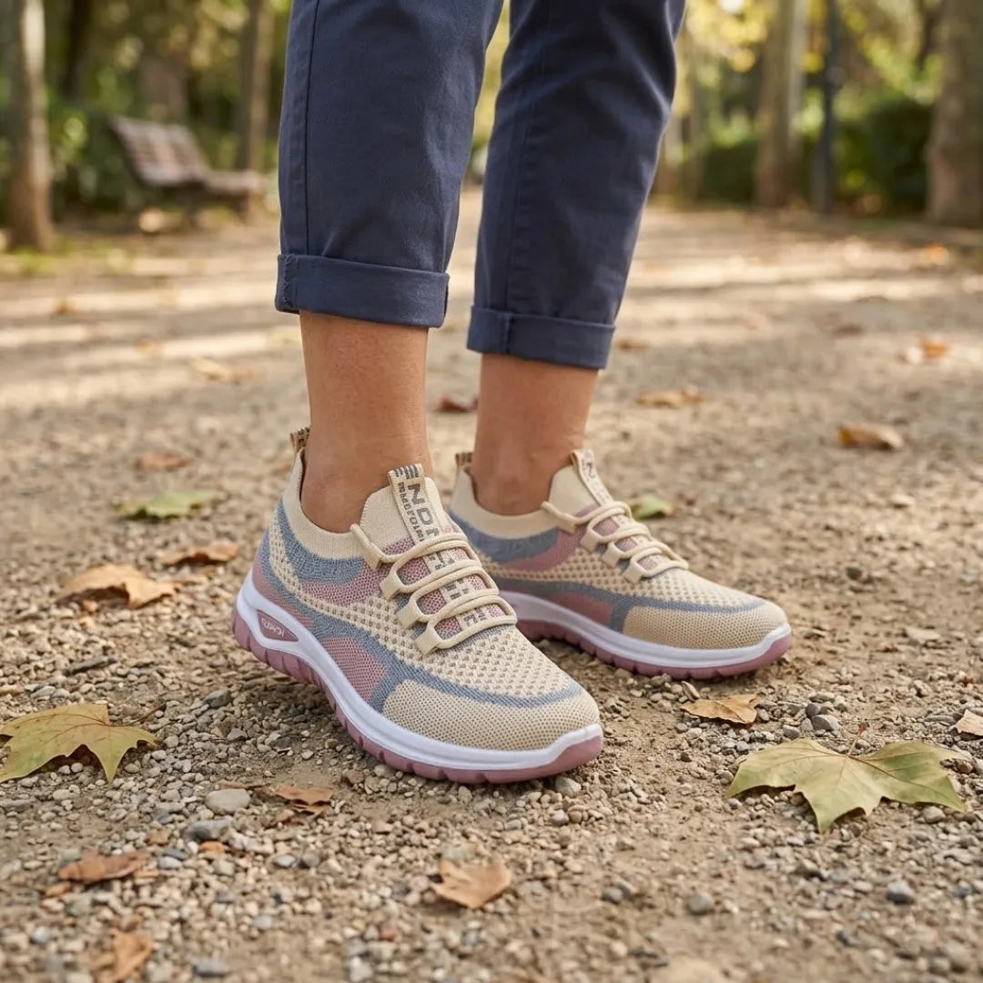 Woman wearing beige, pink and grey mesh trainers with rolled navy trousers, standing on a leafy park path. 29