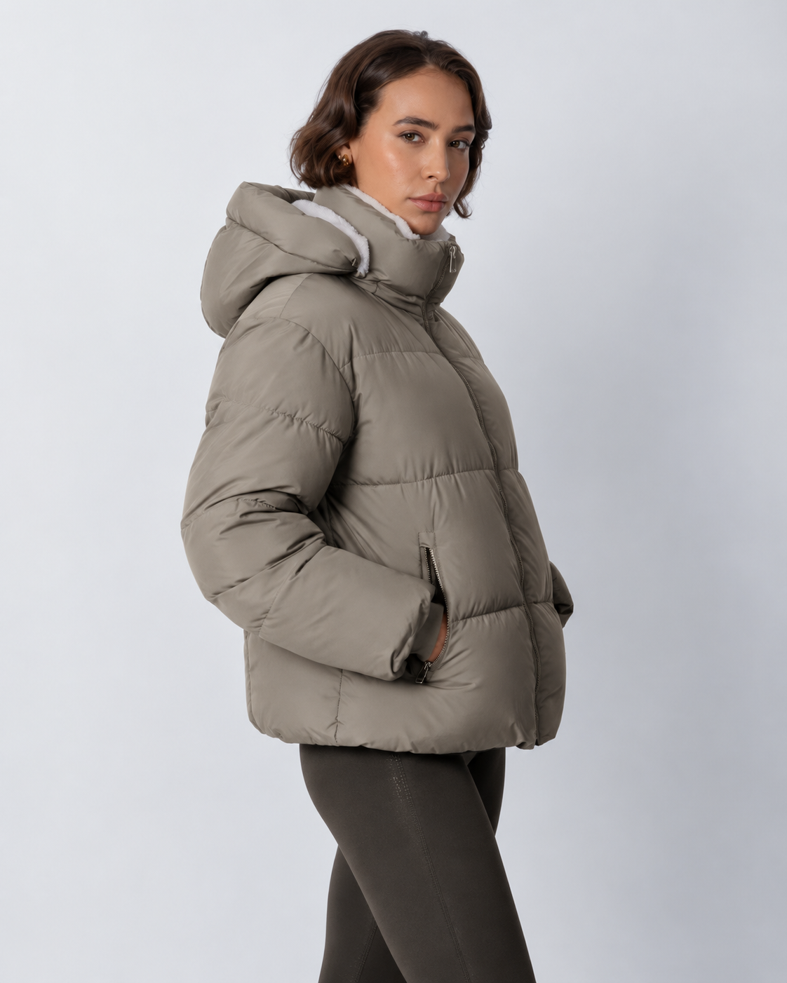 Side view of the taupe-grey puffer jacket with hood up, showing the zipped pocket and quilted sleeves 19