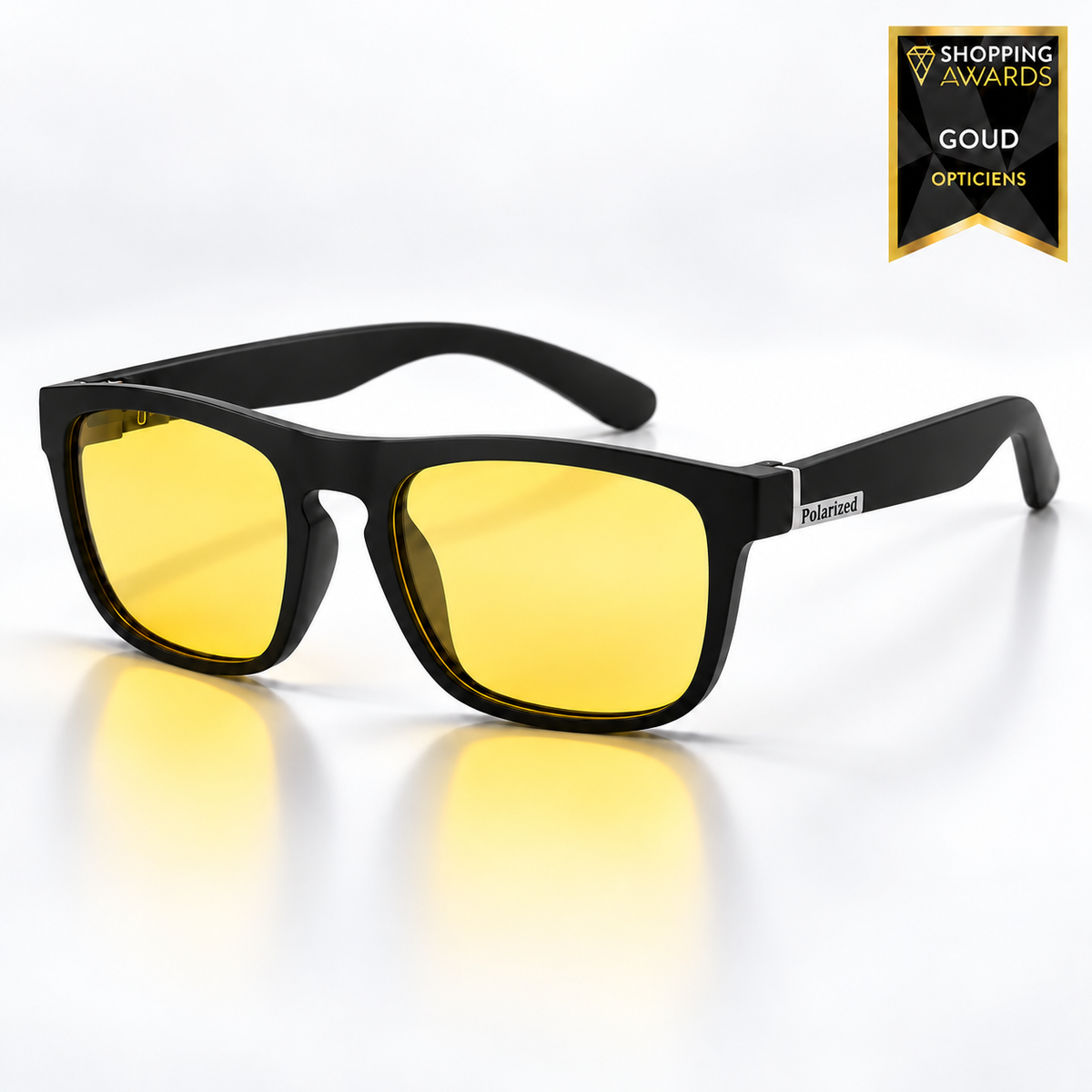 Matte black square-framed glasses with yellow lenses and a small silver label on the arm, shown at an angle on a reflective white surface. 9