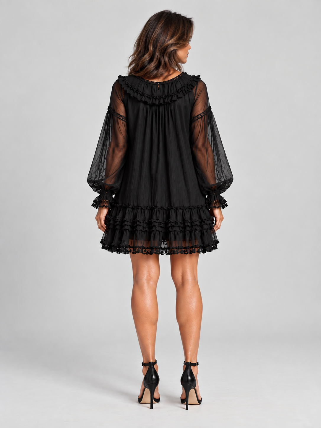 Back view of a model in the black dress, showing the ruffled collar, sheer sleeves and tiered ruffle hem. 4