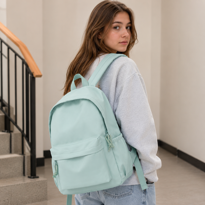 Young woman looking over her shoulder wearing the mint green backpack over a grey sweatshirt and jeans in a stairwell. 3