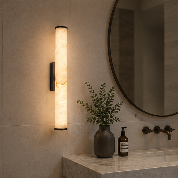 Dark-finished marble wall light glowing beside a round mirror above a marble bathroom vanity with a vase and soap dispenser. 4
