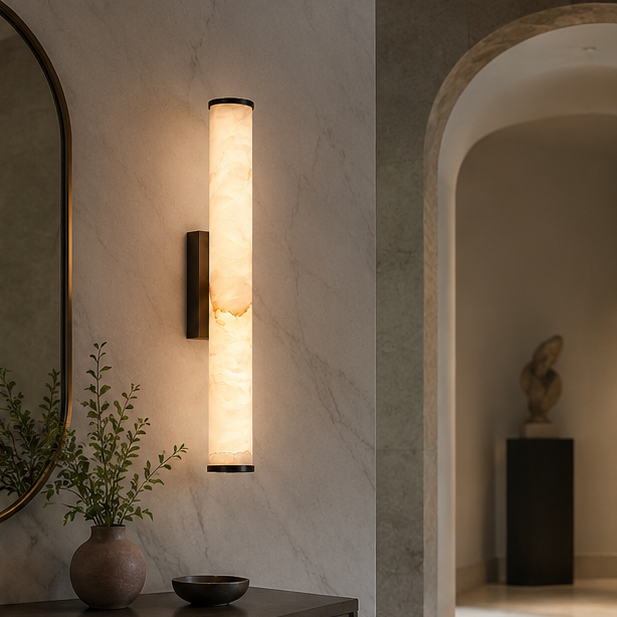 Marble cylinder wall light with dark caps on a veined stone wall in a hallway, with a vase and bowl on a console. 5