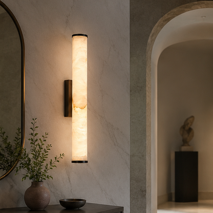 Marble cylinder wall light with dark caps on a veined stone wall in a hallway, with a vase and bowl on a console. 5