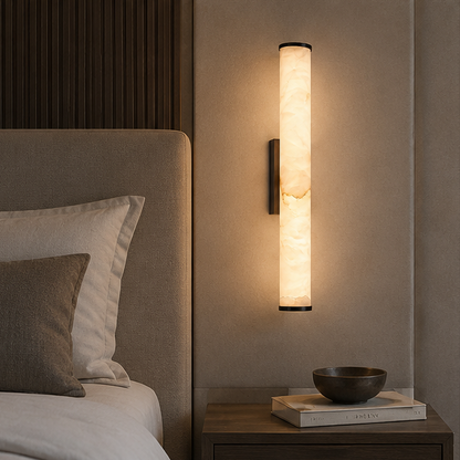 Marble wall light with dark caps glowing beside a upholstered bed as a bedside lamp, above a nightstand with books and a bowl. 6