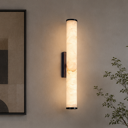 Lit vertical marble wall light with dark metal end caps and bracket, mounted on a neutral wall beside an abstract framed print. 3